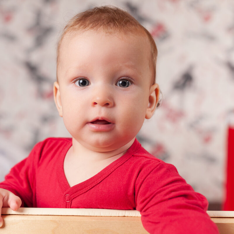 a small child stands and holds the edge of the bed or playpen in the nursery, happy and happy smiling baby, the concept of child development, the first steps, selfie